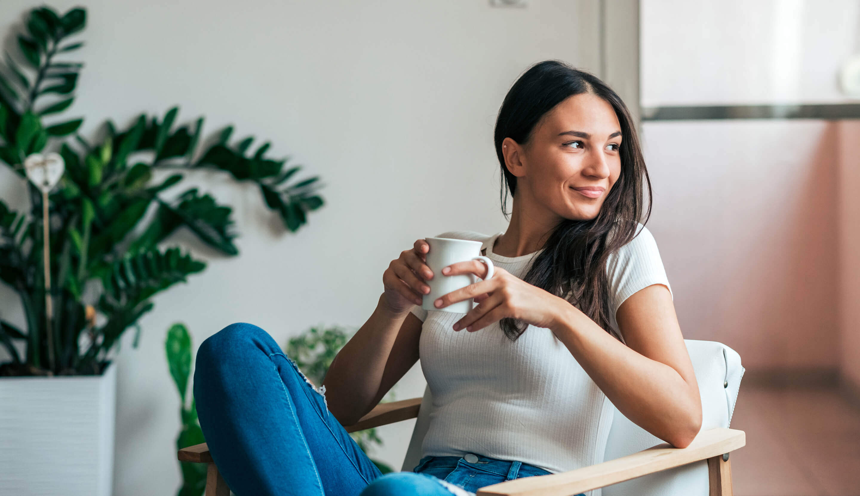 Frau sitzt mit weißer Kaffeetasse im Sessel