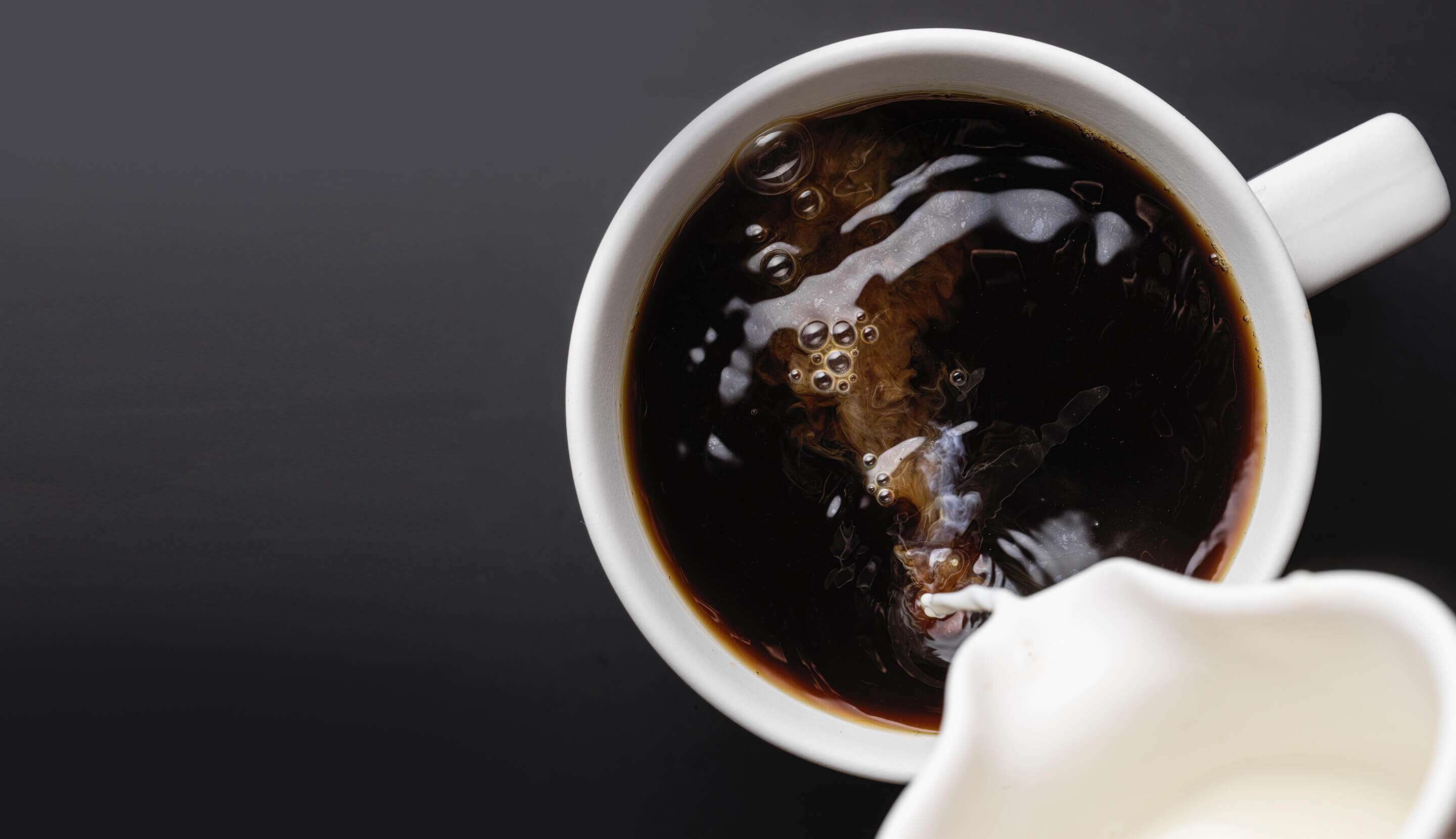 Schwarzer Kaffee in weißer Tasse mit einem Schuss Milch