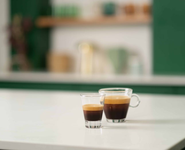 Dvě sklenice stojící na bílém stole - jedna s Starbucks® Ristretto Shot, druhá s Starbucks® Blonde nebo Dark Espresso.