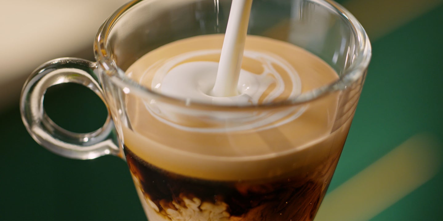 Ein Glas Starbucks Nespresso Kaffee mit dichter goldbrauner Crema, in das ein Kaffeetropfen fällt.