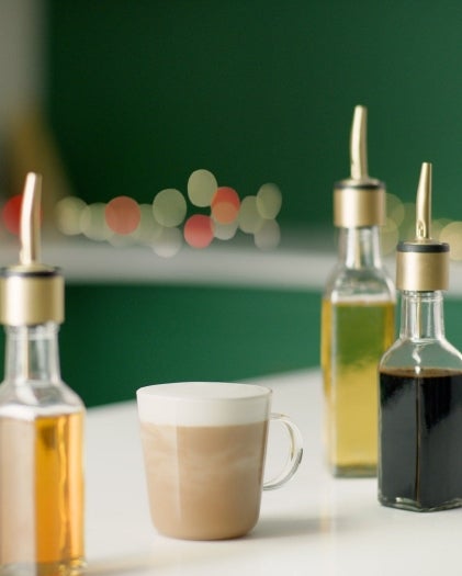 Café sobre una mesa junto a cuatro frascos de sirope