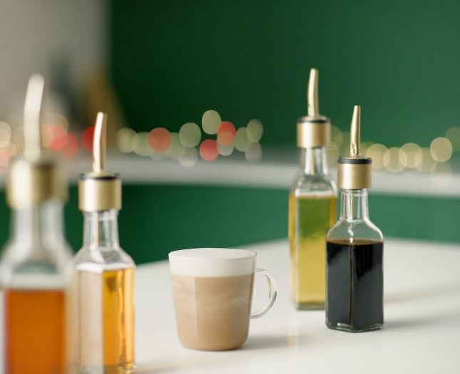 Kaffe på ett bord bredvid fyra sirapsflaskor