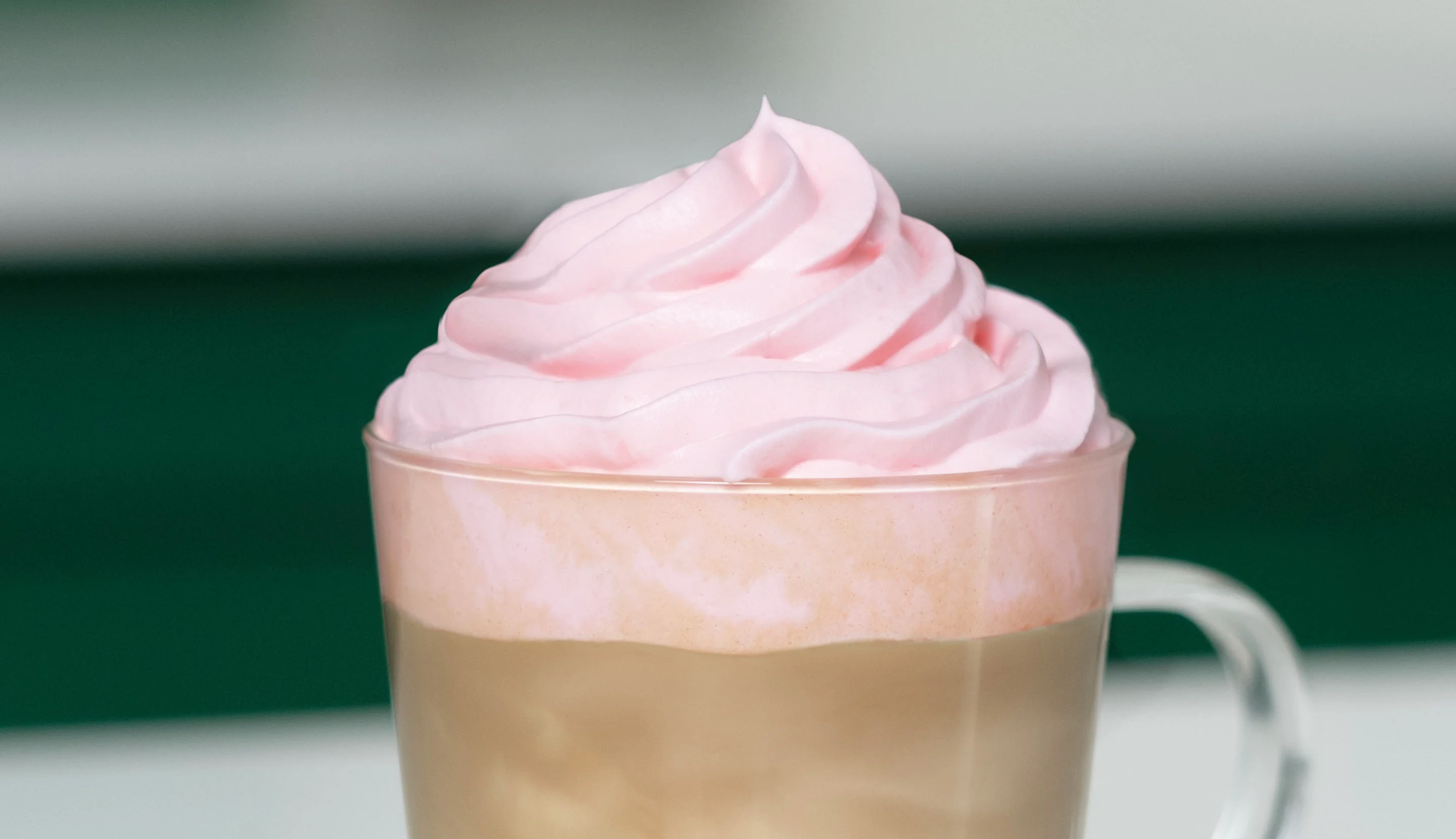 Pink whipped cream is piped onto a layered coffee for a decorative finish.
