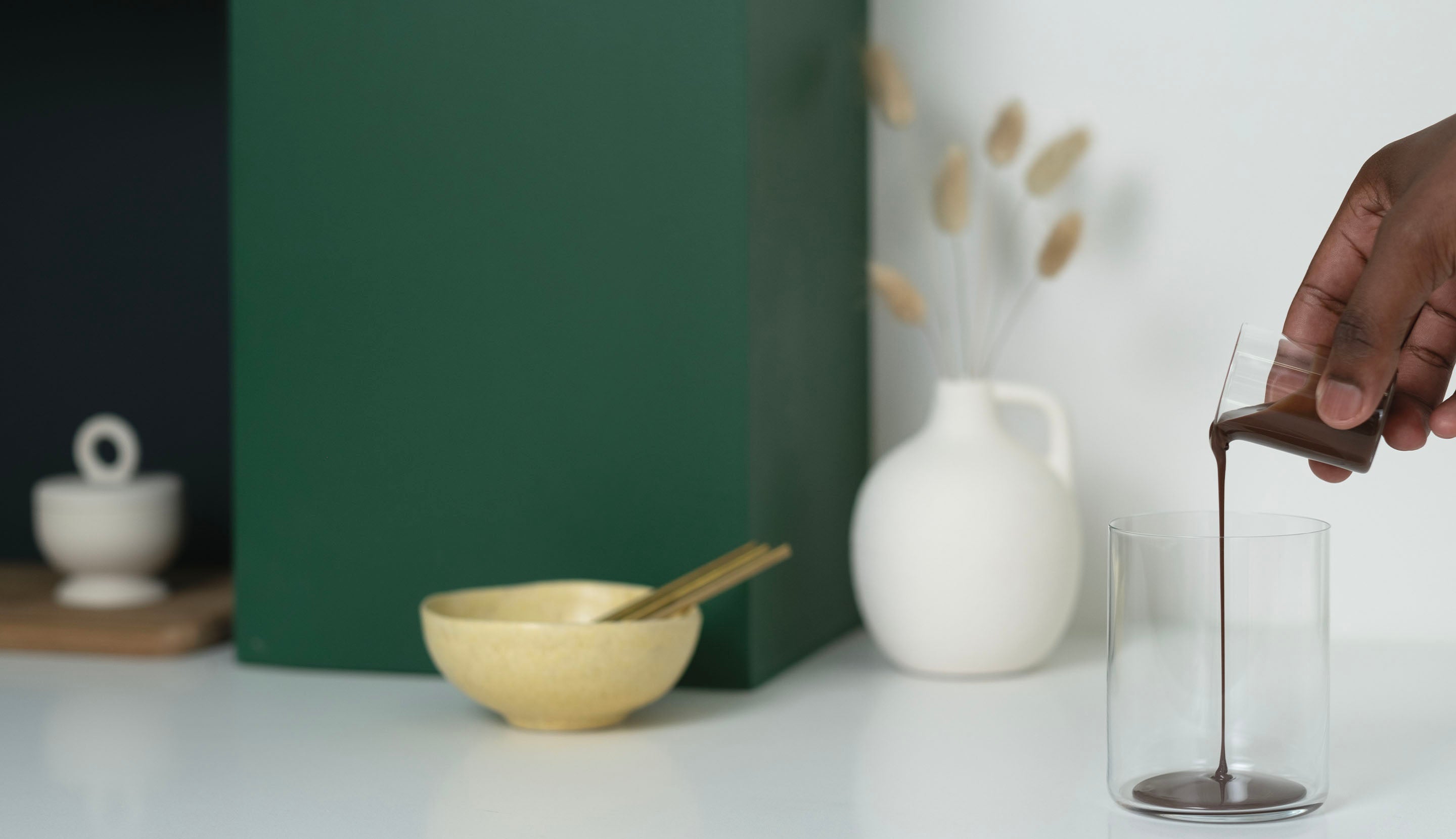 A hand pours chocolate sauce into an empty glass.