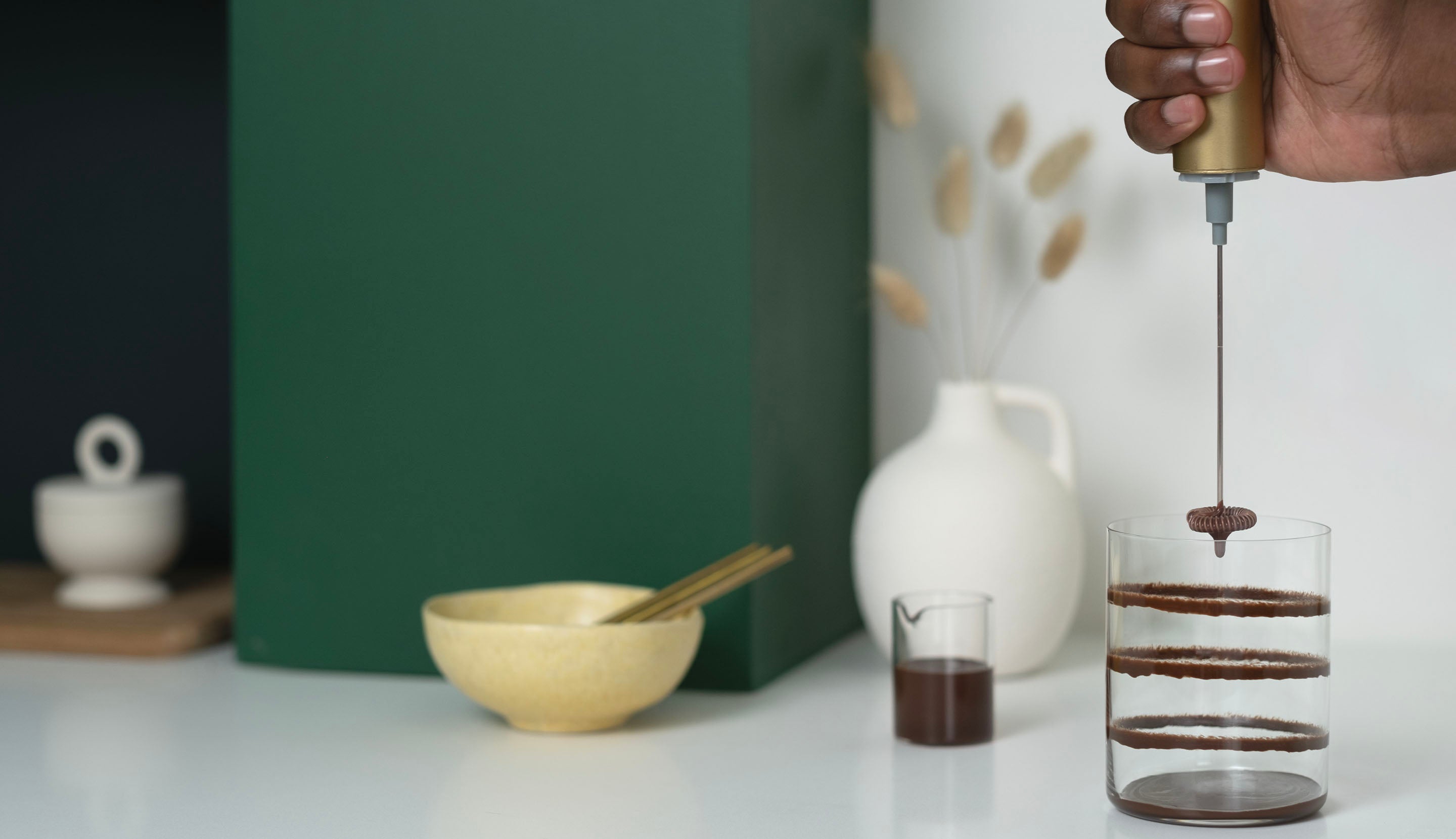 A handheld frother creates rings of chocolate sauce inside a clear glass.