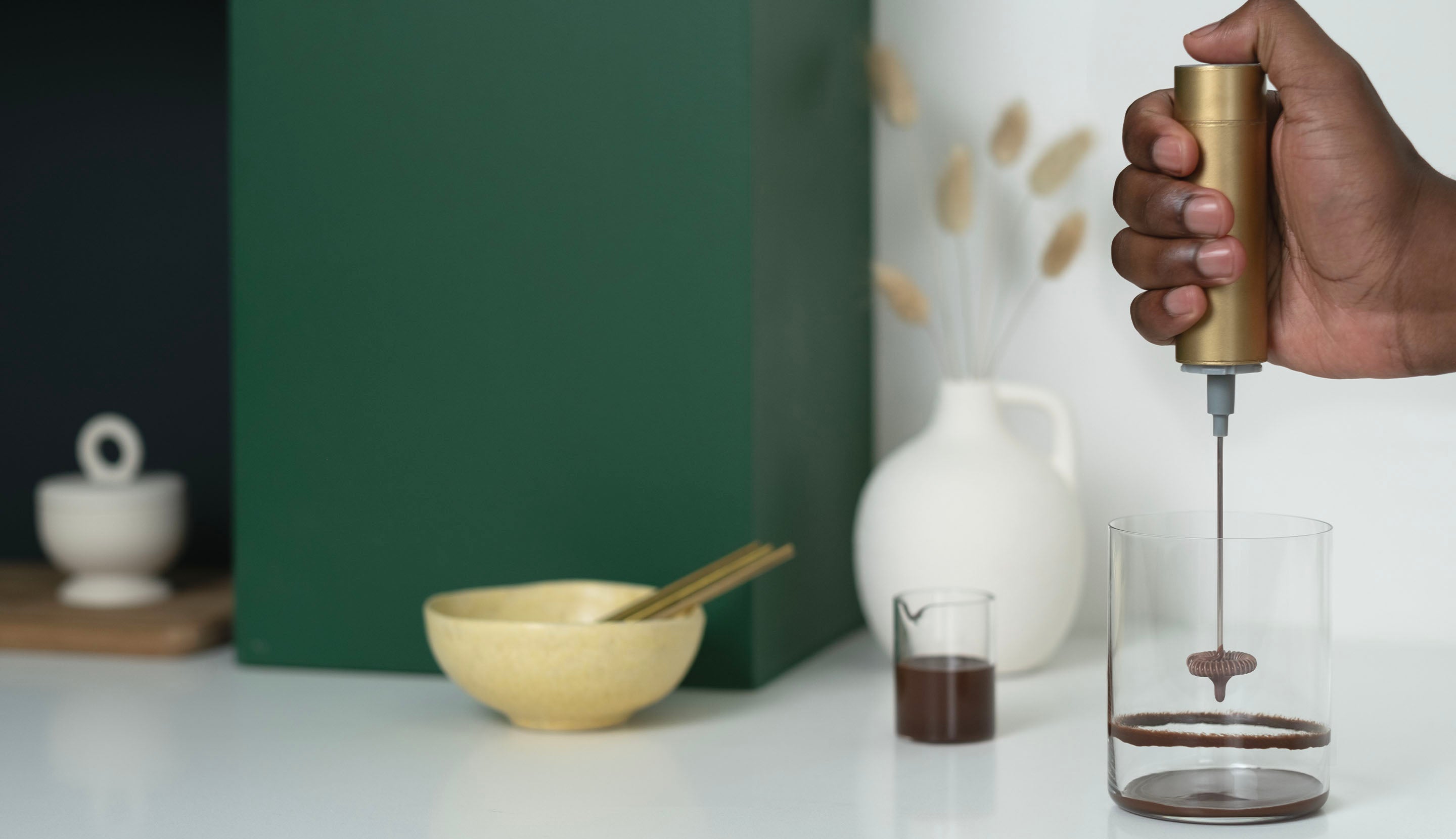 A handheld frother creates chocolate rings around the inside of a clear glass.