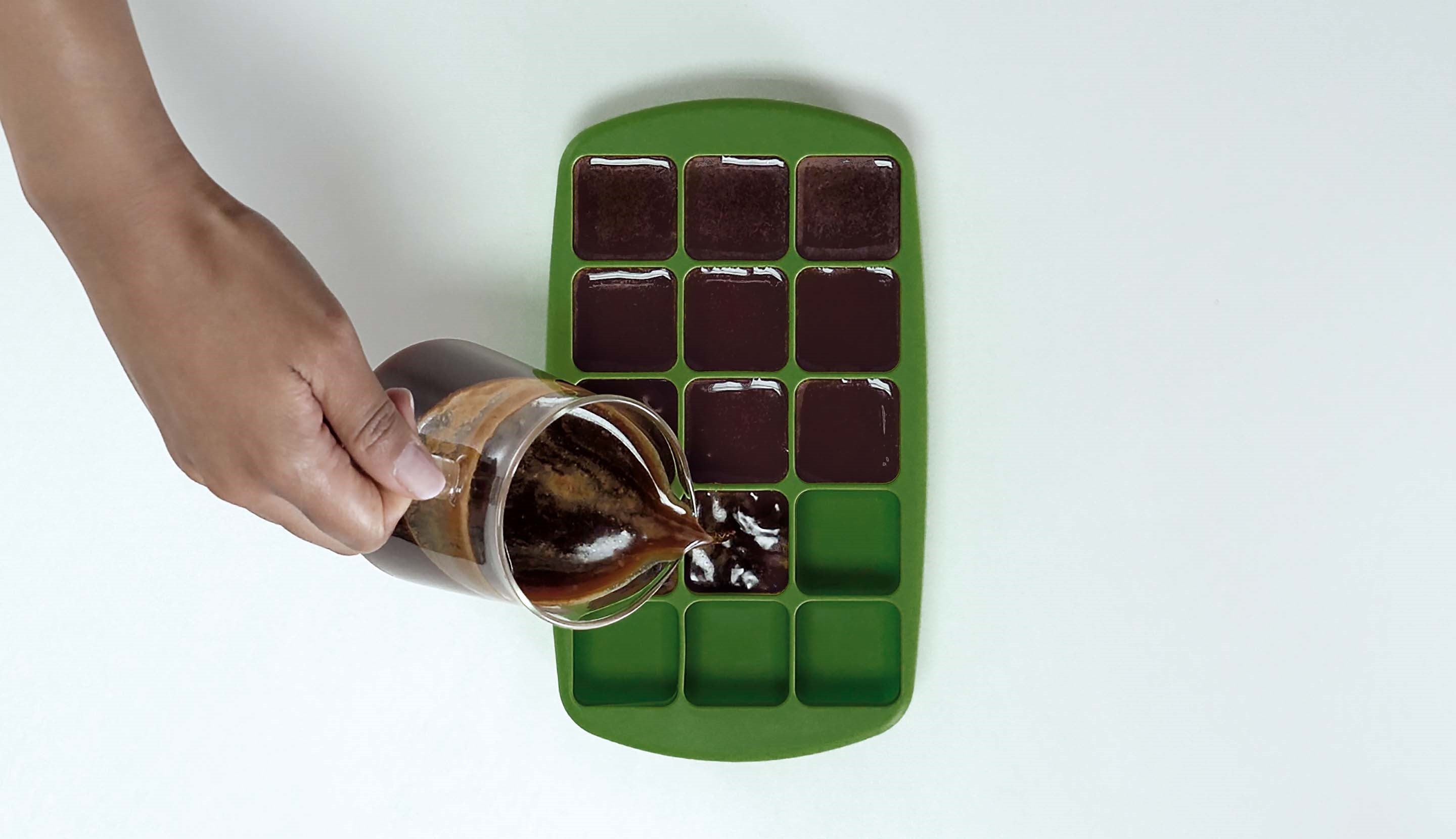 Pouring freshly brewed Starbucks® coffee into an ice cube tray.