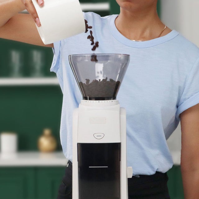 woman poring coffee beans in a coffee grinder