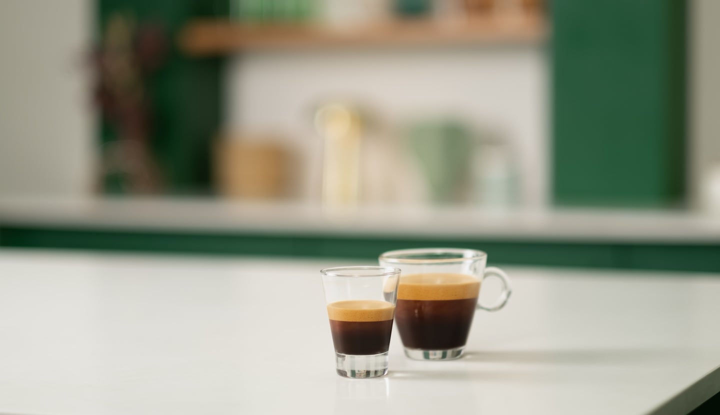 Two glasses standing on the white table - one with Starbucks® Ristretto Shot, another with Starbucks® Blonde or Dark Espresso