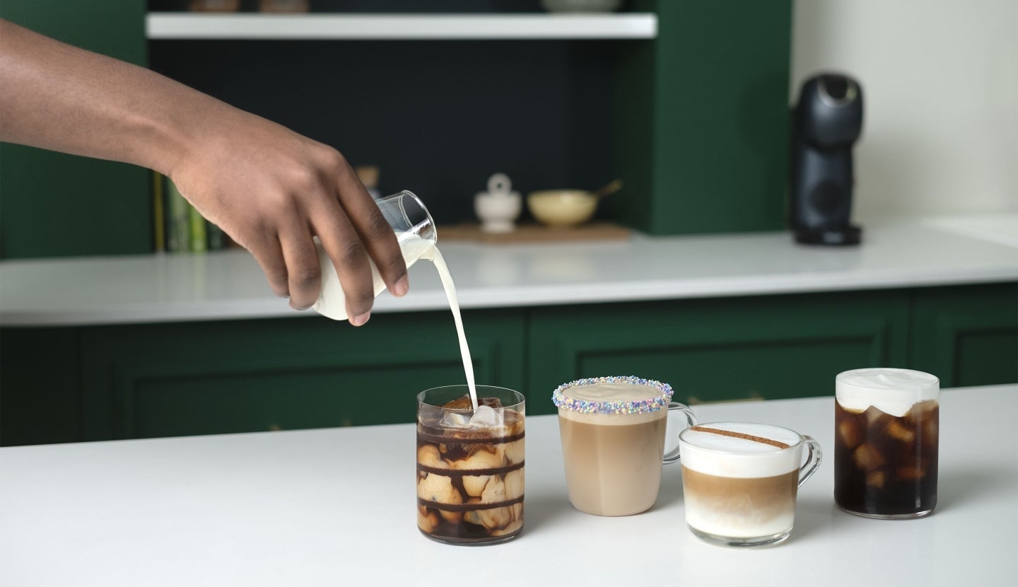Four coffee drinks with different toppings, as milk is poured into an iced coffee with chocolate syrup.