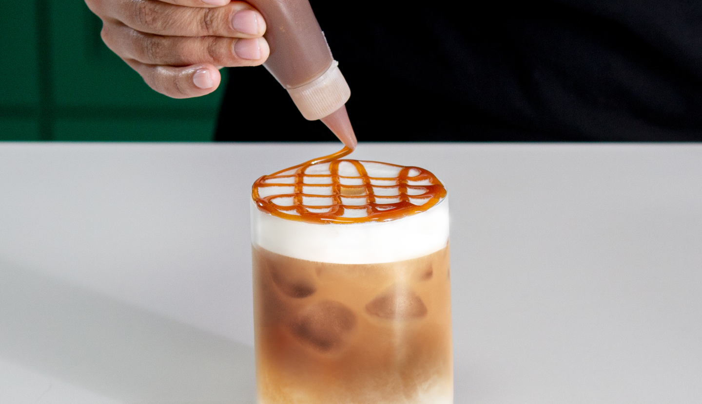 Caramel sauce being drizzled over the foam of an iced Starbucks® coffee.