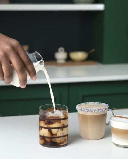 Four coffee drinks with different toppings, as milk is poured into an iced coffee with chocolate syrup.