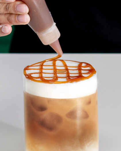 Caramel sauce being drizzled over the foam of an iced Starbucks® coffee.