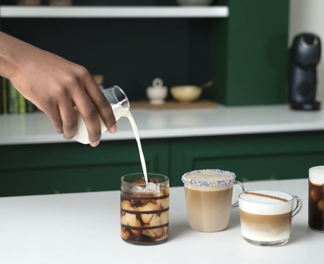 Four coffee drinks with different toppings, as milk is poured into an iced coffee with chocolate syrup.