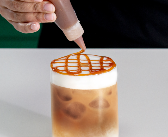 Caramel sauce being drizzled over the foam of an iced Starbucks® coffee.
